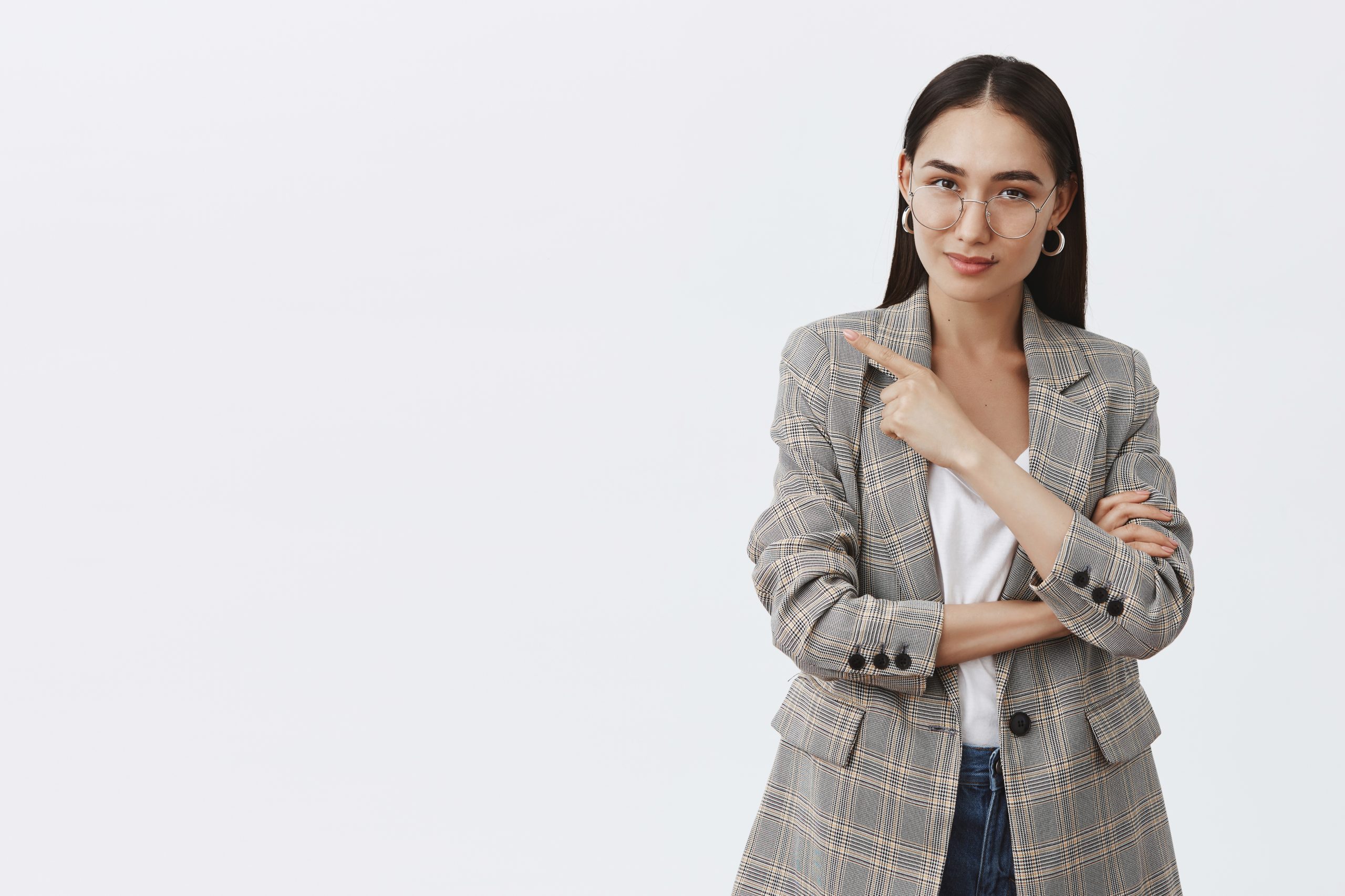 Come and look at my new car. Portrait of good-looking intrigued female journalist in glasses and jacket over t-shirt, pointing left and gazing curiously at camera, having some interesting intention.